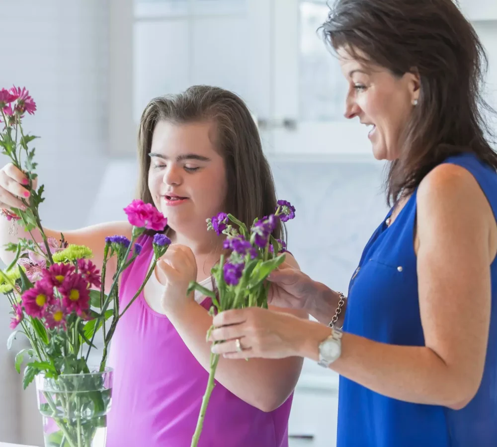 Disabled girl with carer putting flowers in a vase